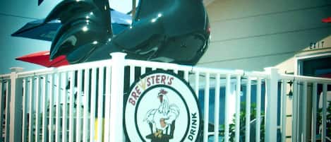 A restaurant sign with a rooster logo and the words "BRESTER'S FINE FOOD AND DRINK" on a white fence.