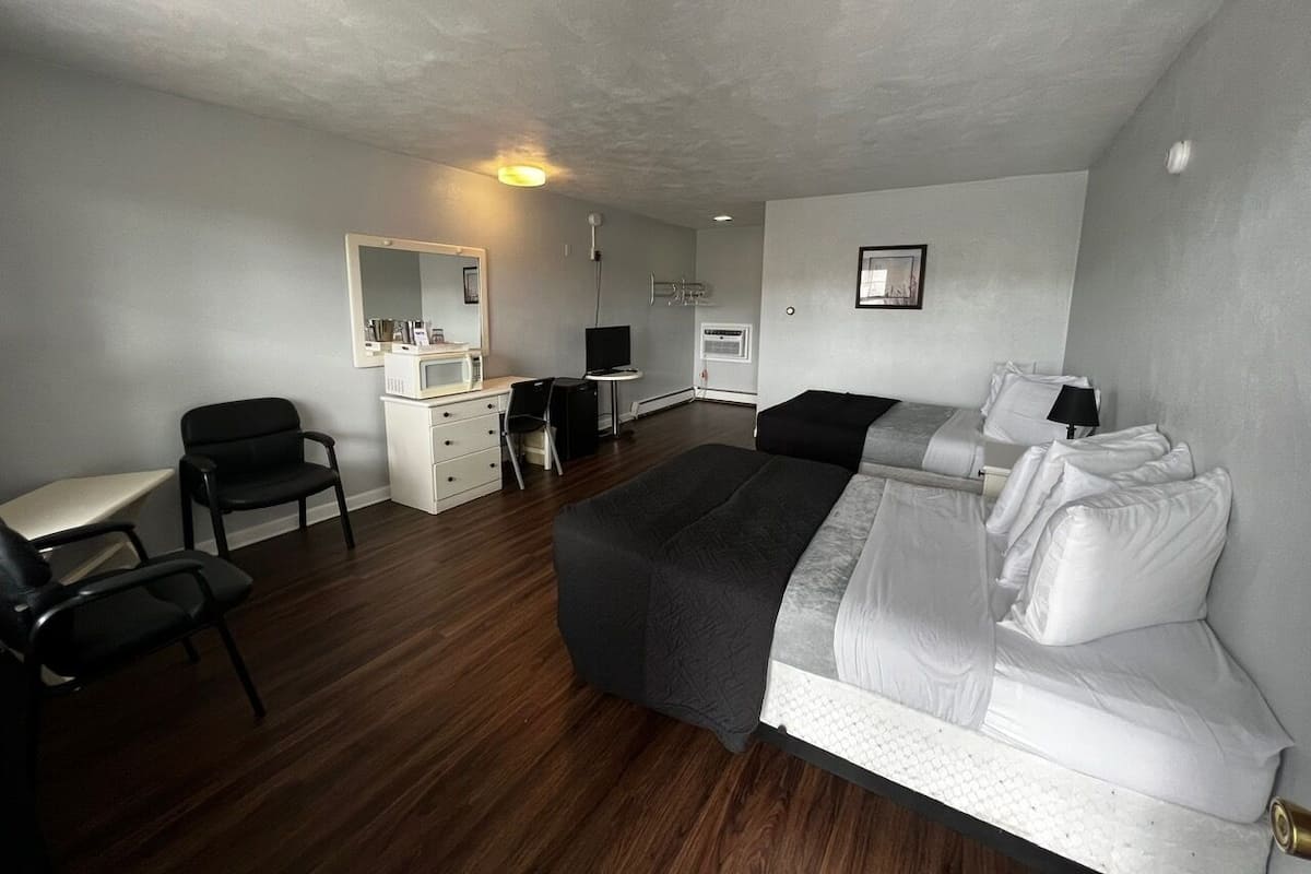 A hotel room with a bed, a desk, a chair, a small kitchenette, and a mirror.