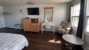 A hotel room with a bed, a desk with a chair, a microwave, a TV, a large mirror, and a window with curtains.