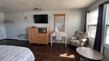 Habitación de hotel con cama, escritorio con silla, microondas, televisor, espejo grande y ventana con cortinas.