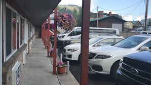 A row of hotel rooms with a covered outdoor area, a parking lot with several cars, and a mountain in the background.