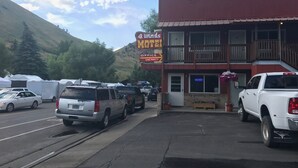 A motel with a red exterior and a balcony on the second floor. There are several cars parked in front, and a sign indicating vacancy.