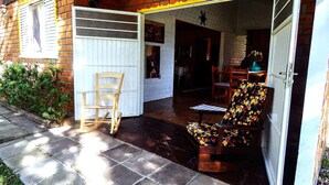 A patio area with a wooden rocking chair and a floral armchair, a brick wall, and a white door leading to an interior space. - Chale Charm Gramado (Gramado)