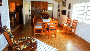 A dining area with wooden furniture, a kitchen in the background, and a brick wall. - Chale Charm Gramado (Gramado)