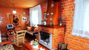 A cozy living room with a brick fireplace, wooden furniture, and a television on a small table. - Chale Charm Gramado (Gramado)