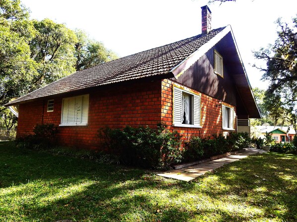 A red brick house with a sloped roof, white shutters, and a chimney.