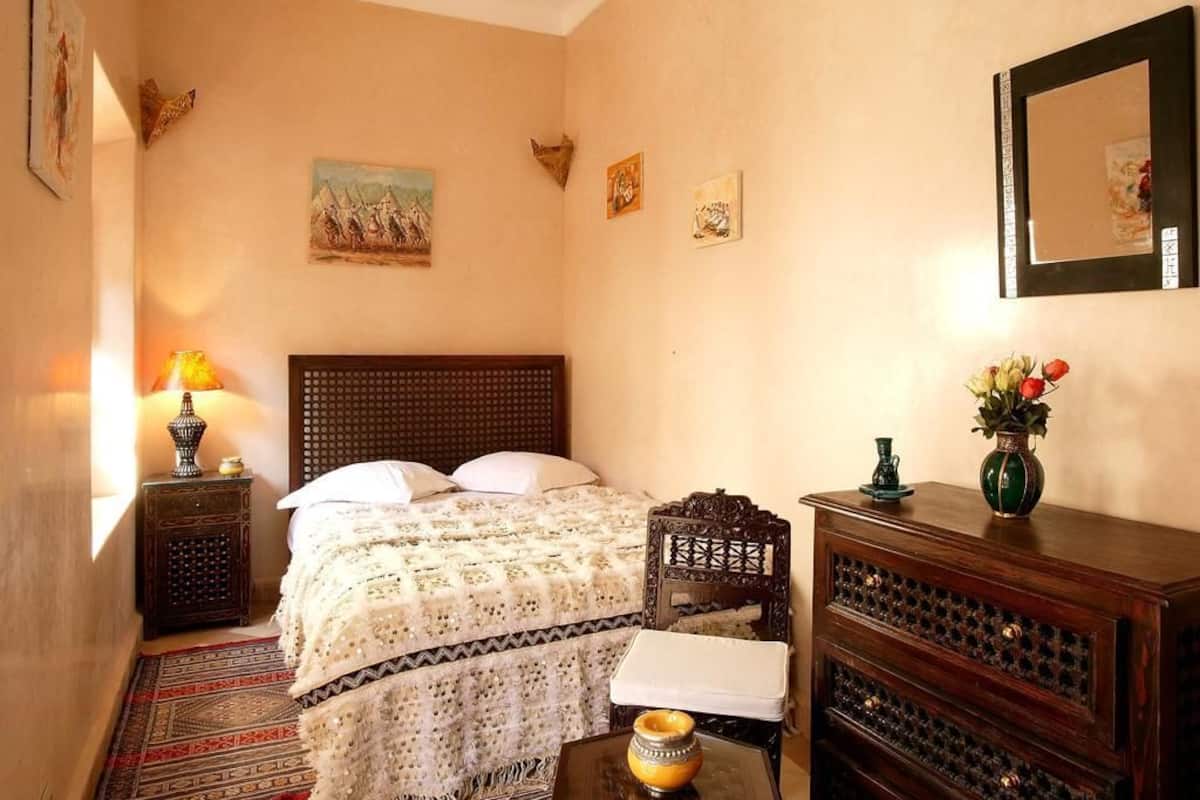 A neatly arranged bedroom with a bed, bedside table, dresser, and a mirror on the wall.