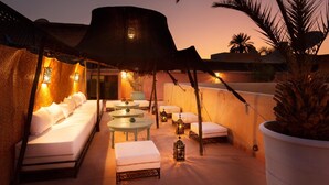 Une terrasse sur le toit aménagée avec un lit, des chaises longues, des tables et des lanternes.