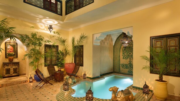 Un espace piscine intérieur luxueux, doté d’un sol à carreaux, entouré de plantes en pot et de lanternes décoratives.