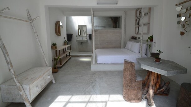 A modern bedroom with a large bed, a wooden bench, a small table, and a mirror. - Radio Tulum Hotel (Tulum)