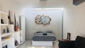 A modern bedroom with a bed, a chandelier, a wall art piece, and a bookshelf. - Radio Tulum Hotel (Tulum)