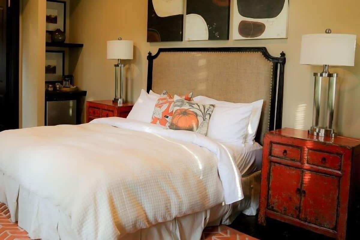 A neatly arranged bedroom with a bed, bedside tables, a nightstand, a dresser, a mirror, and a microwave.