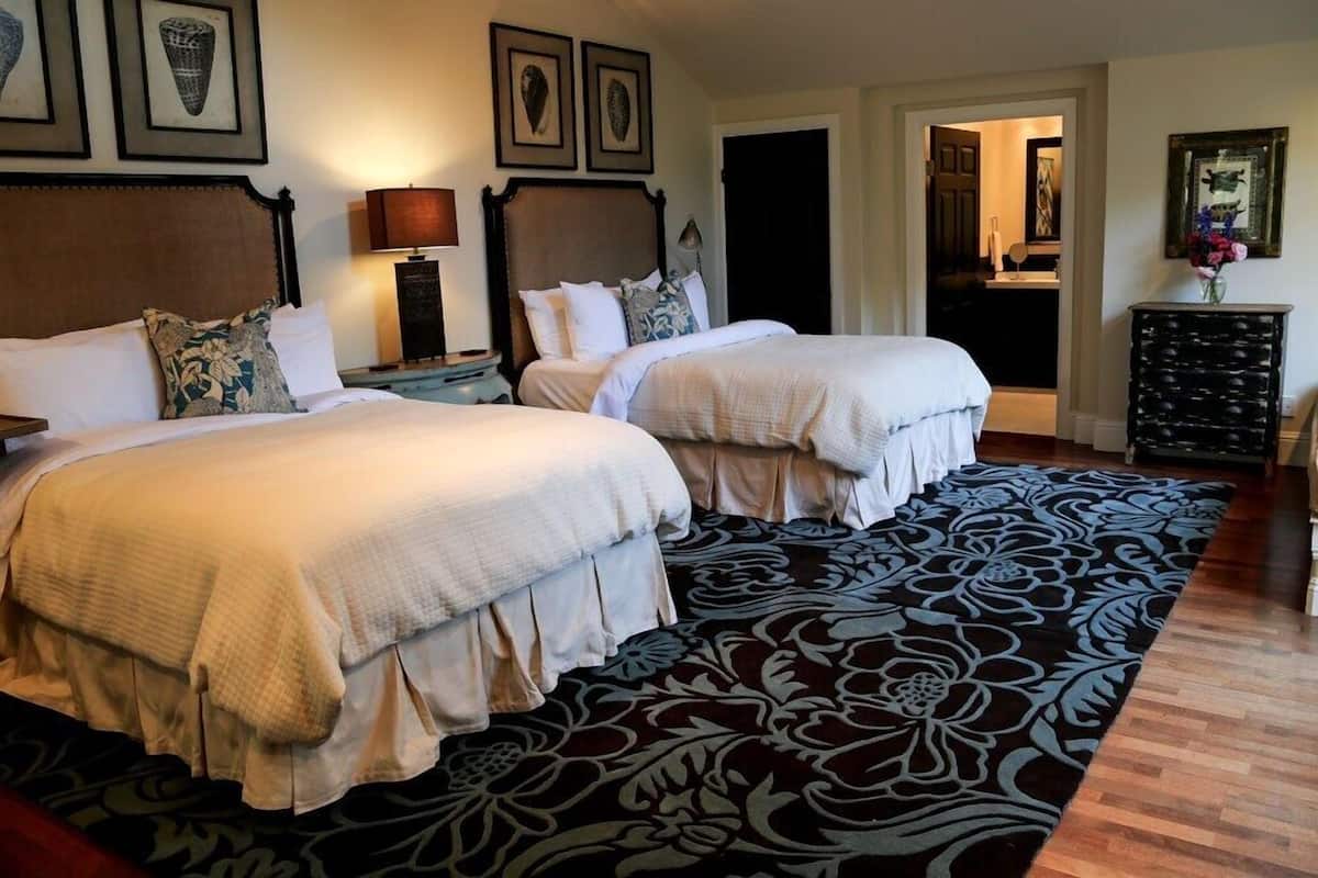 A hotel room with two beds, a large patterned rug, and artwork on the walls.
