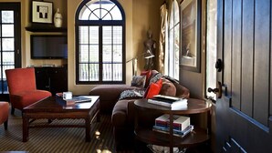 A cozy living room with a large arched window, a red armchair, a brown sofa, and a coffee table.
