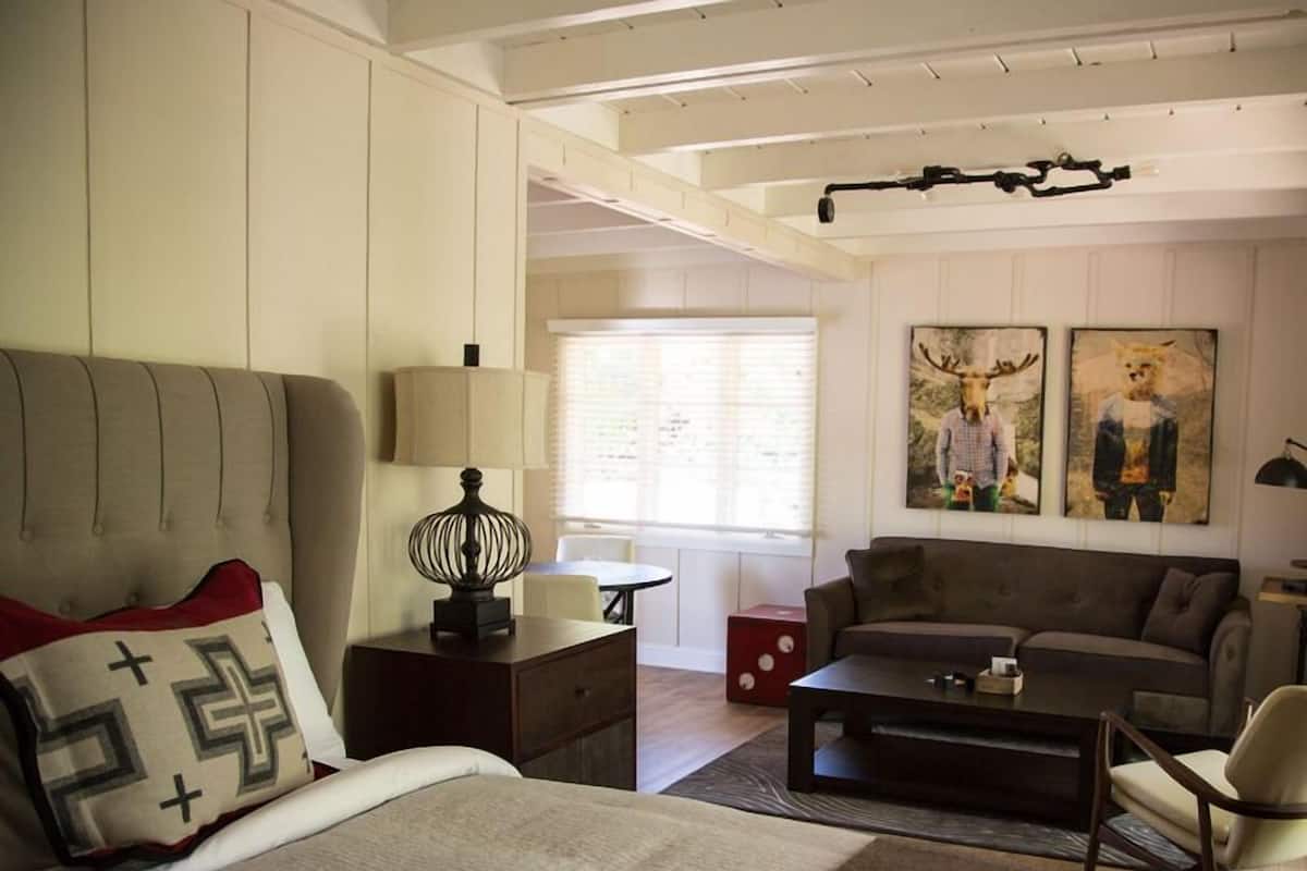 A modern bedroom with a large bed, a sofa, and a coffee table. There is a lamp on a nightstand and a painting on the wall.