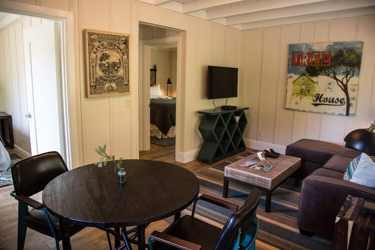 A cozy living room with a round table, a sofa, a TV, and a painting on the wall.