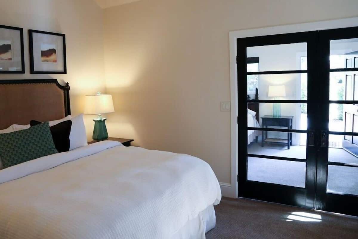 A hotel room with a bed, a nightstand, a lamp, and a door leading to an outdoor area.