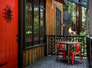 A wooden deck with a red door and black-framed windows, a small table, and two red chairs. - The Madrones (Philo)