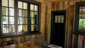 A wooden-paneled room with a table and chairs, a black door, and windows with blinds.