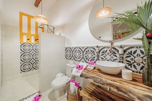 A bathroom with a white toilet, a large sink, and a mirror above the sink. There is a wooden countertop and a plant on the right side.