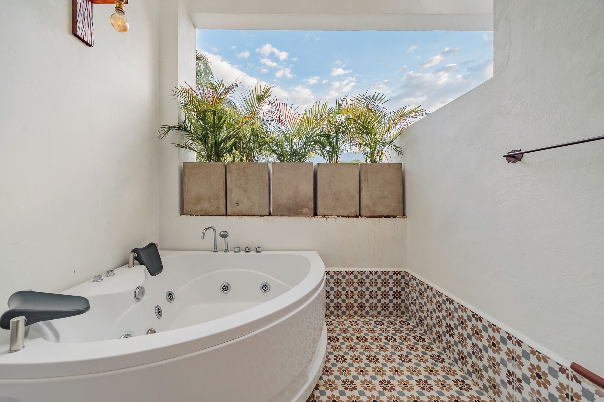 Un baño con una bañera independiente, un ventanal con vistas a palmeras y suelo de baldosas.