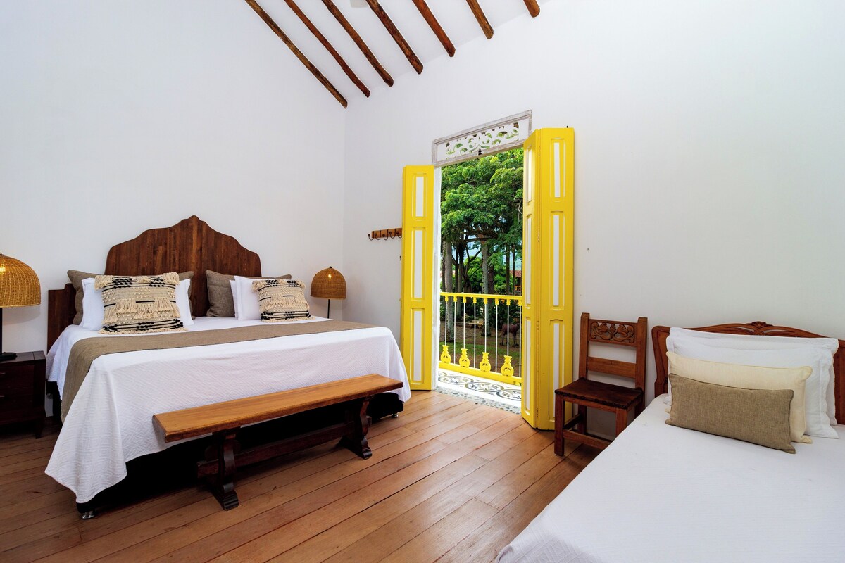 A bedroom with a bed, a bench, a chair, and a door leading to an outdoor area.