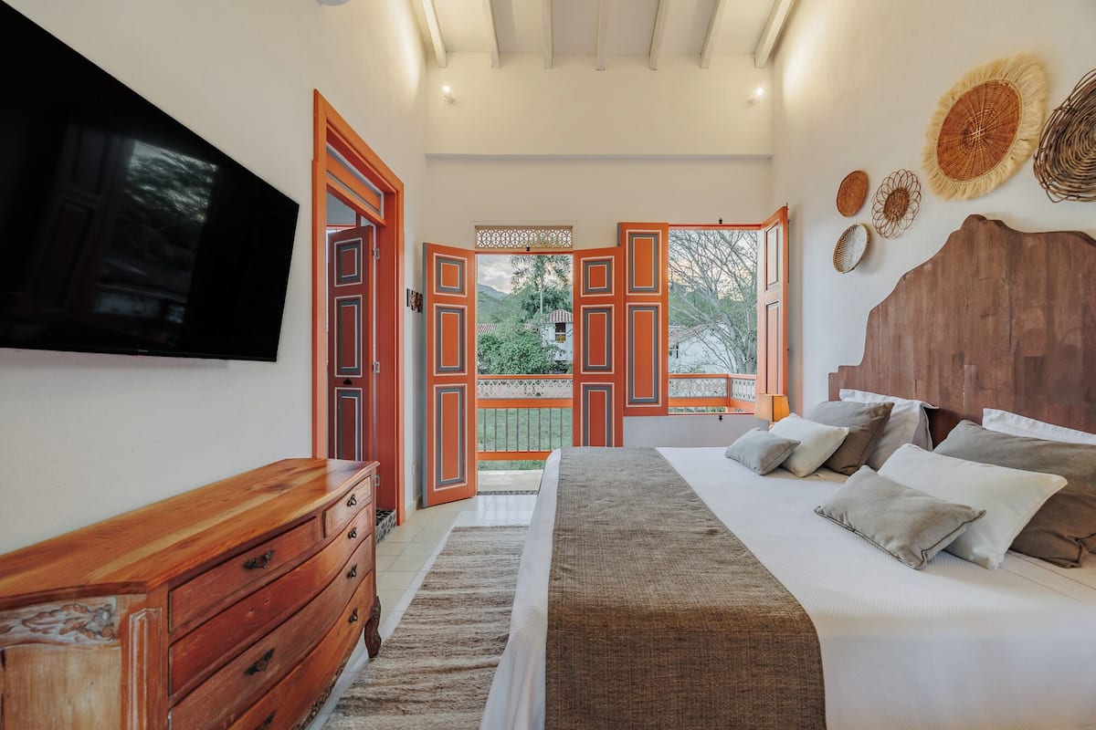 A bedroom with a large bed, wooden dresser, and a TV mounted on the wall.