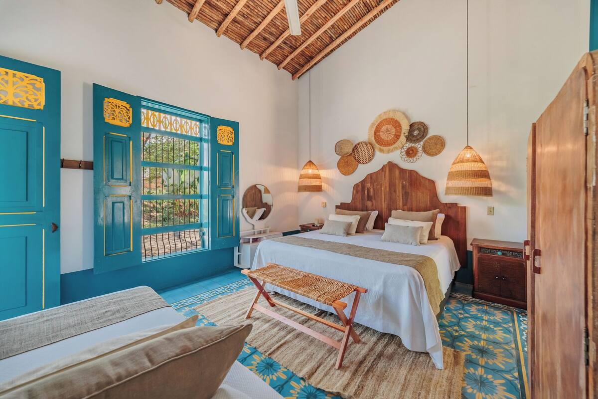 A bedroom with a bed, bedside tables, a bench, a wardrobe, and a window with decorative panels.