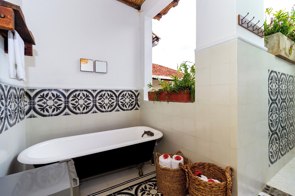 A bathroom with a bathtub, tiled walls, a hanging plant, and a basket with towels.