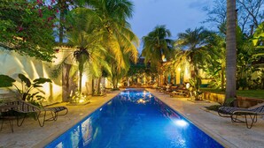 Uma piscina com espreguiçadeiras, cercada por palmeiras e plantas tropicais.