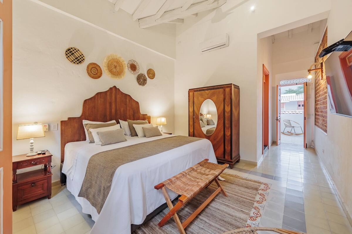 A bedroom with a wooden bed, bedside tables, a mirror, and a view of the outside.