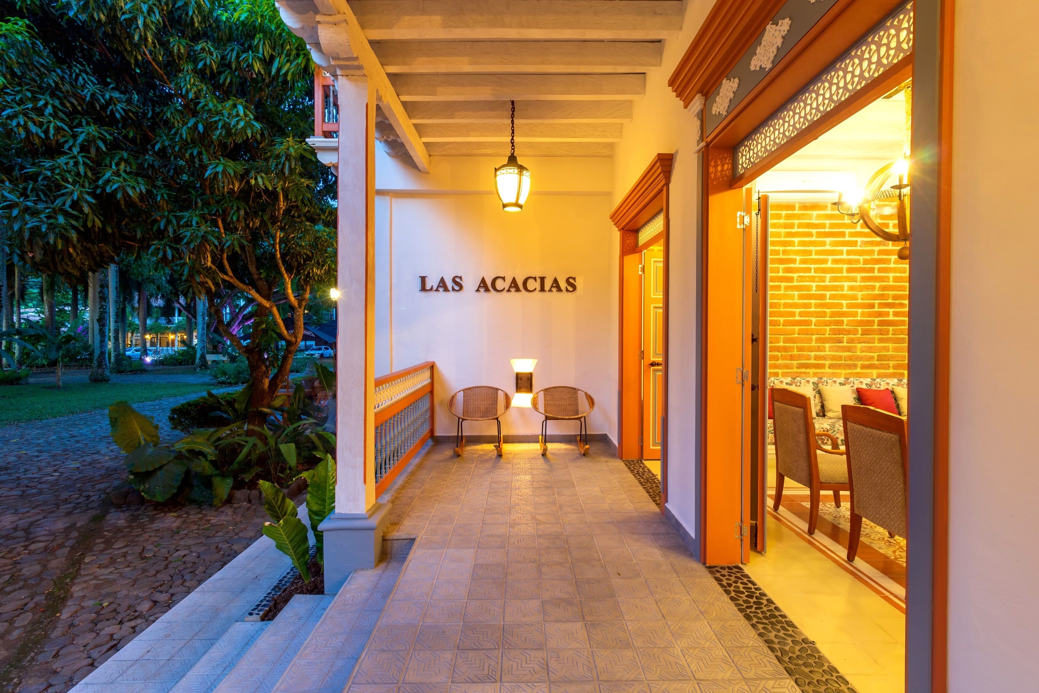 A corridor with a sign reading "LAS ACACIAS," two wicker chairs, and a brick wall with a door.