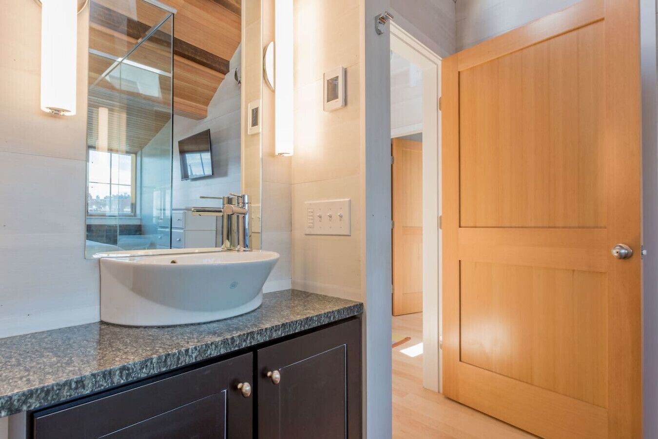A modern bathroom with a freestanding sink, a mirror, and a wooden door.