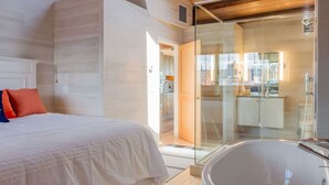 Un dormitorio moderno con una cama grande, cabina de ducha con paredes de vidrio y vista a la ciudad.