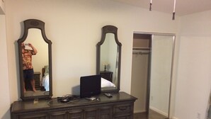 A bedroom with a dark wooden dresser, a flat-screen TV, and a full-length mirror.