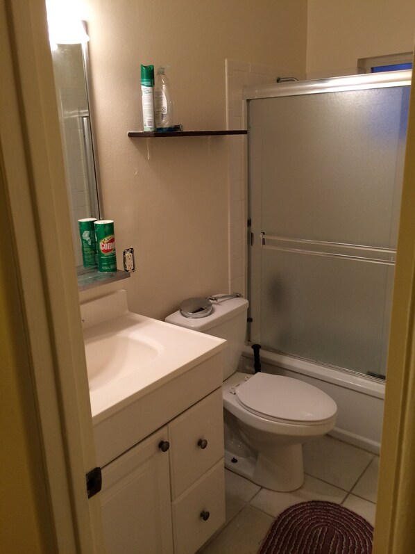 Een badkamer met toilet, wastafel en douche. Er staan schoonmaakmiddelen op de plank.