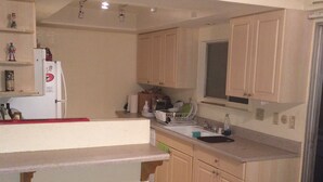 A kitchen with light wooden cabinets, a white countertop, a refrigerator, and a window above the sink.