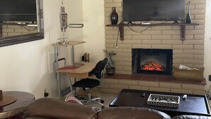 A living room with a fireplace, a mounted TV, a desk with a chair, and a leather sofa.