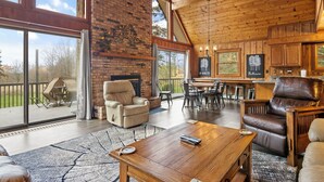 Amplia sala de estar con chimenea, sillones de cuero, una mesa de madera y ventanas grandes que ofrecen vistas al exterior.