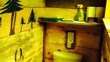 Een compacte houten badkamer met toilet, een klein plankje met toiletartikelen en een muurdecoratie van bomen.