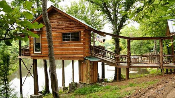 A wooden cabin on stilts over a body of water, with a deck and railing. - 1 BEDROOM 1 BATH, TREE-CABIN BY A 20 ACRE PRIVATE LAKE (Jackson)