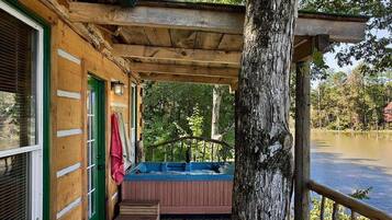 Una cabaña de madera con un jacuzzi en un muelle de madera, con vista a un cuerpo de agua.