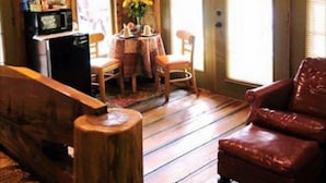 A cozy cabin interior with wooden walls, a dining area with a table and chairs, a red leather chair, and a television mounted on the wall. - 1 BEDROOM 1 BATH, TREE-CABIN BY A 20 ACRE PRIVATE LAKE (Jackson)