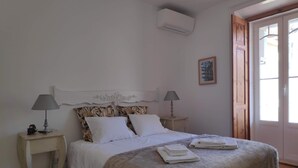 A bedroom with a bed, two bedside tables with lamps, a wall-mounted air conditioner, and a door with a window. - In the heart of the Portuguese capital (Lisboa)