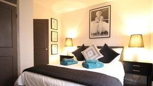 Una cama bien hecha con edredón blanco y negro, dos toallas azules y un cuadro en la pared.