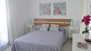 Een slaapkamer met een bed, twee nachtkastjes, een houten hoofdbord en twee bloemrijke wanddecoraties.