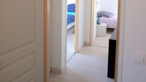 Un couloir menant à une chambre à coucher, où se trouvent un lit, une table de chevet et une lampe.