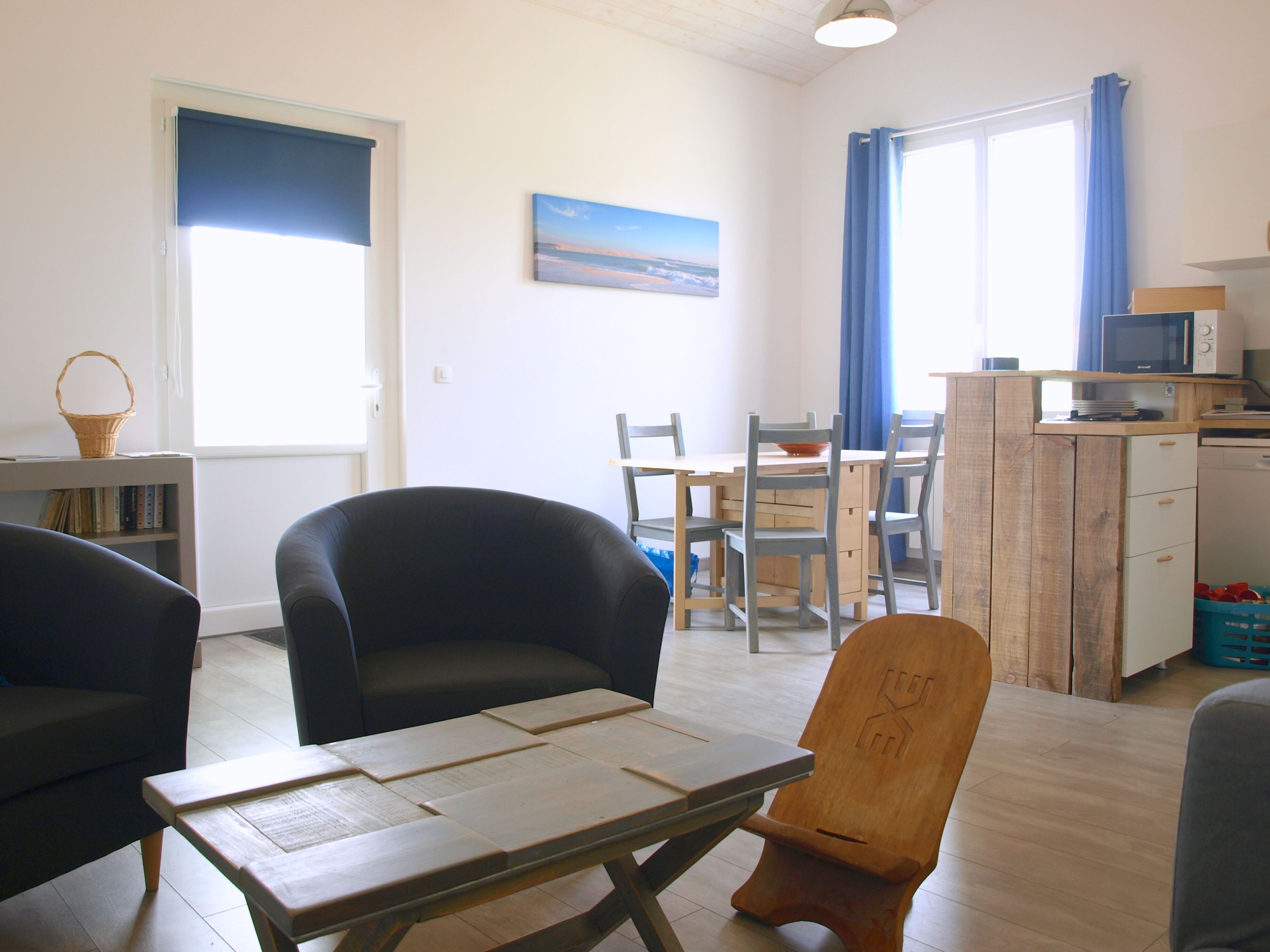 A living room with a wooden table, two chairs, a bookshelf, and a painting on the wall.