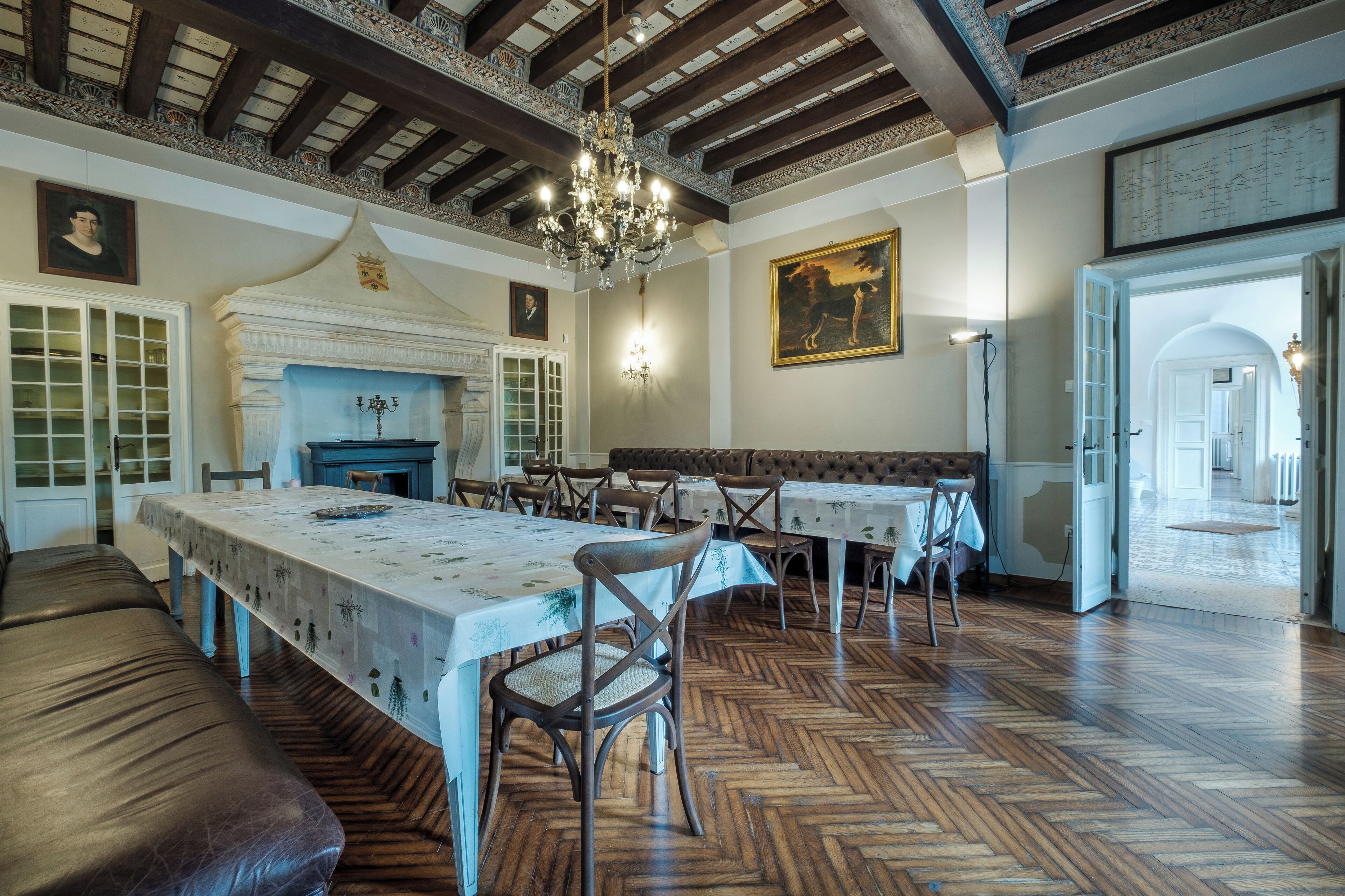 Un espace repas doté d’un plancher en bois, d’une longue table recouverte d’une nappe et d’un lustre.