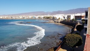 A coastal cityscape with a beach, buildings, and mountains in the background.